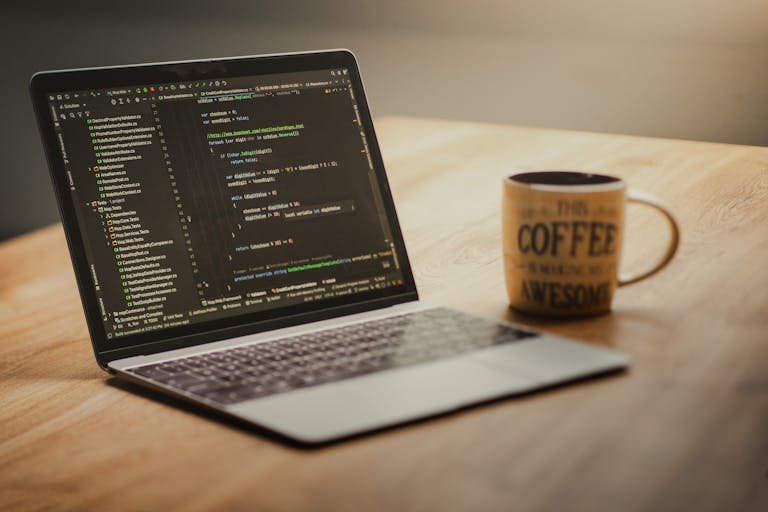 Laptop displaying code editor on a desk with a coffee mug beside it, suggesting a workspace or home office setting.